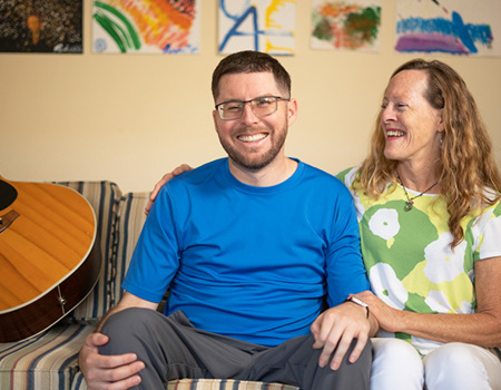 Wounded warrior Richard Ottum and his mother and caregiver Mary Scibona sit on a couch smiling. 