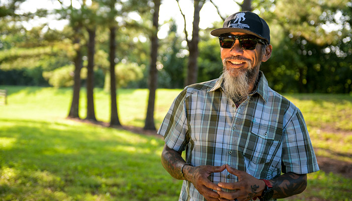 Wounded warrior Ray Andalio standing in a park, smiling and wearing sunglasses and a WWP hat.