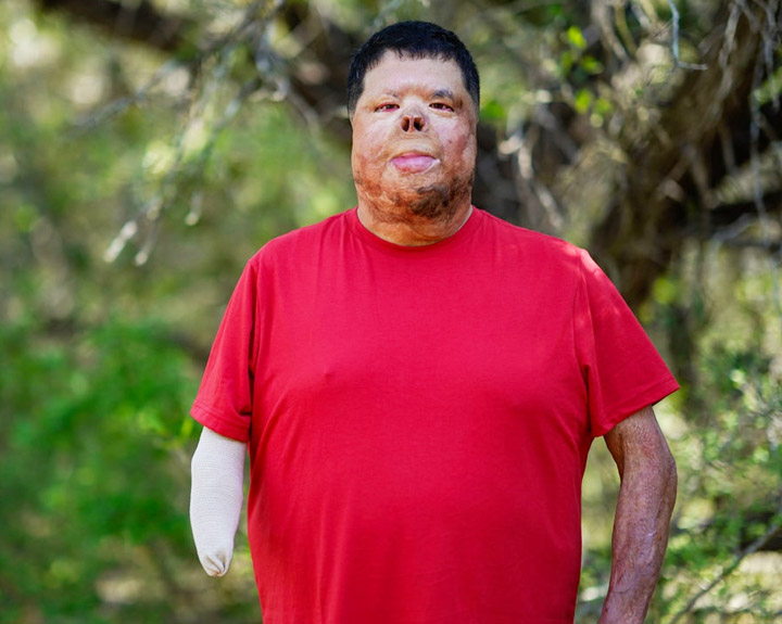 Wounded warrior Anthony Villareal stands outside, wearing a red shirt and smiling at the camera.