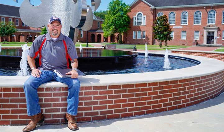 Warrior and peer support group leader Deron Santiny sits on the wall of a large fountain at the University of Louisiana Lafayette.