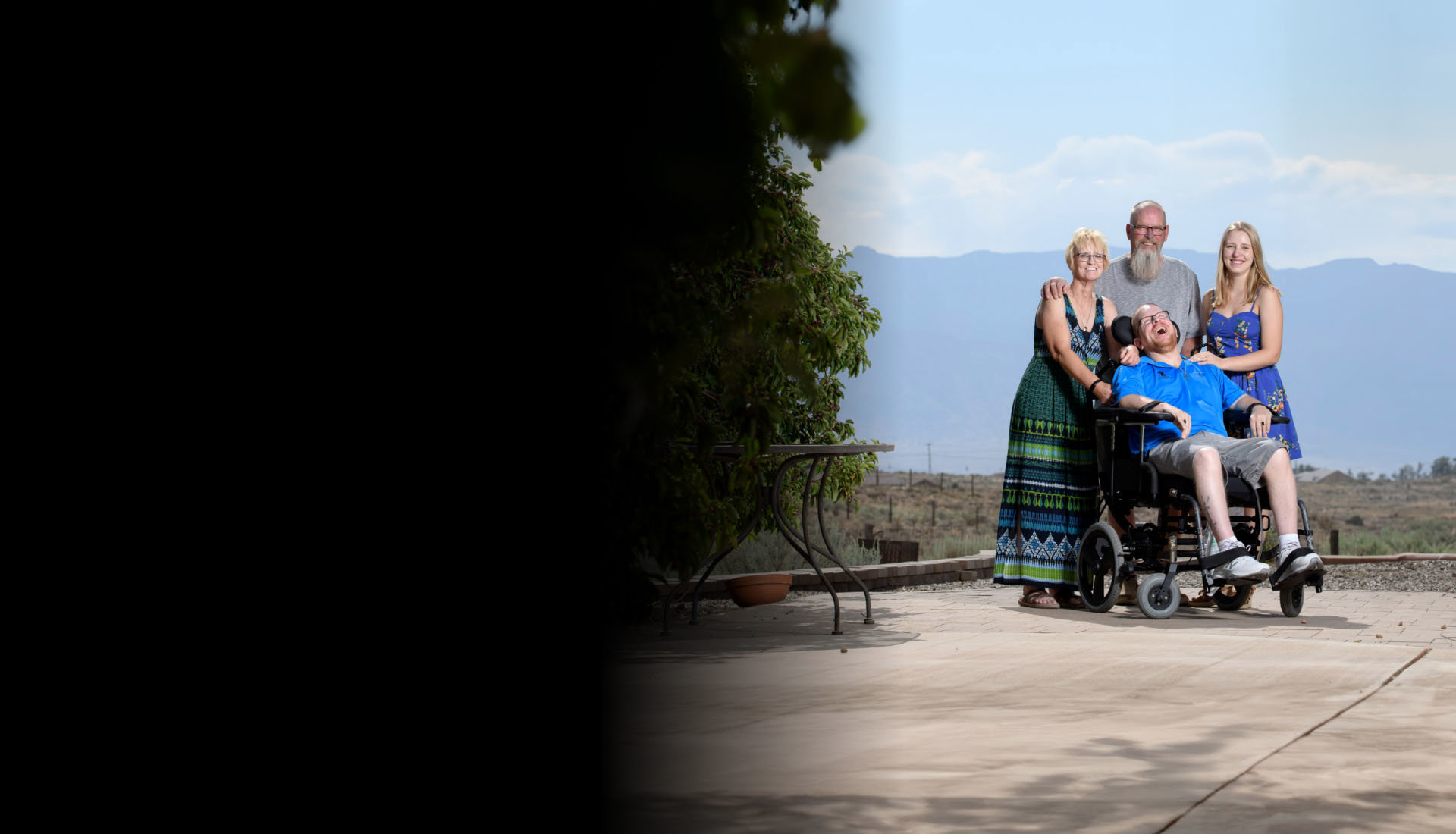 Warrior Erik Schei smiling while in his wheelchair surrounded by his family. They are outside with mountains behind them.