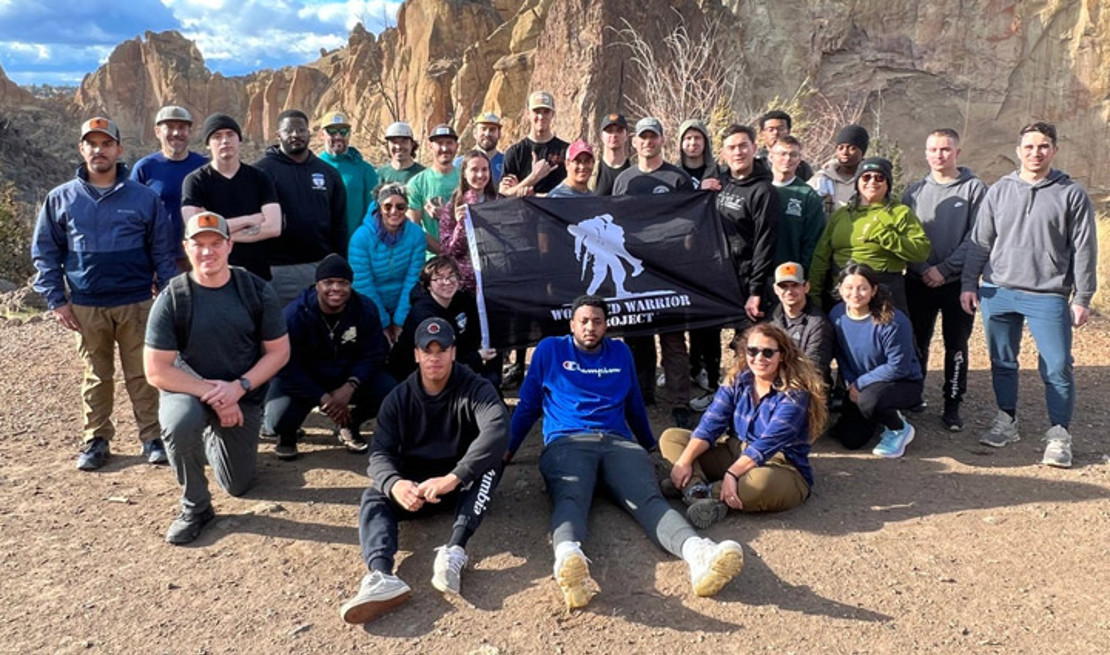 A group of active-duty service members pose together holding a Wounded Warrior Project flag after hiking.
