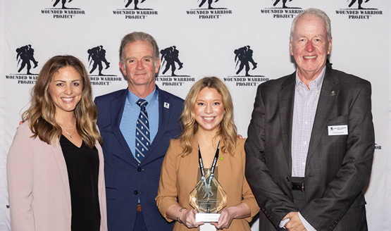 Parker’s Kitchen executive Lauren Burel holding the WWP award stands between WWP Staff Alexis Long and CEO Walt Piatt on the left and Chief Chris Needles on the right.