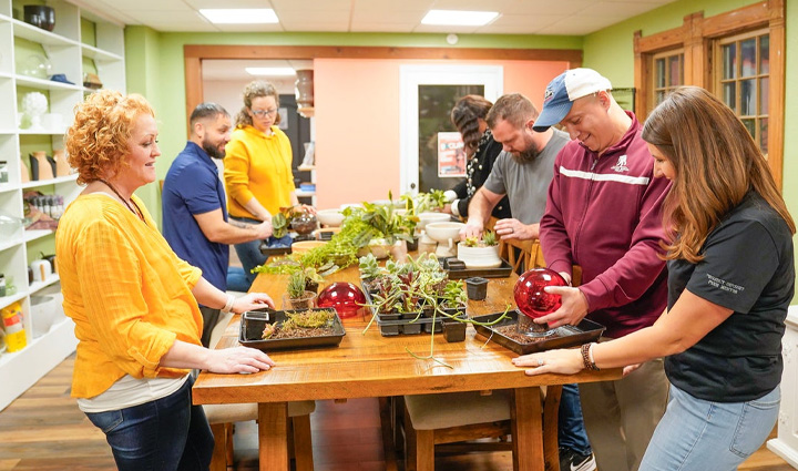 Wounded warriors Dawn Bonebrake, Nathan Covey, Laura Jennings, Camella Andrews, Chris Kallas, Brent Whitten, and Keara Torkelson are around a table, smiling in a plant-growing workshop.