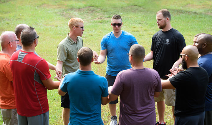A group of wounded warriors stand in a circle while holding hands. 