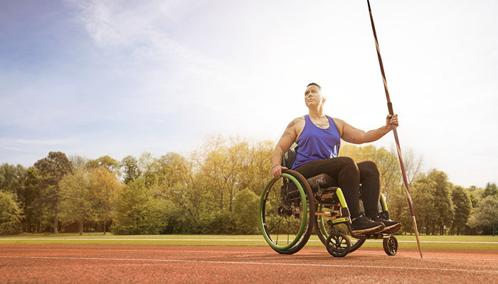 Wounded warrior Beth King sitting in a wheelchair and holding a javelin on a track field.