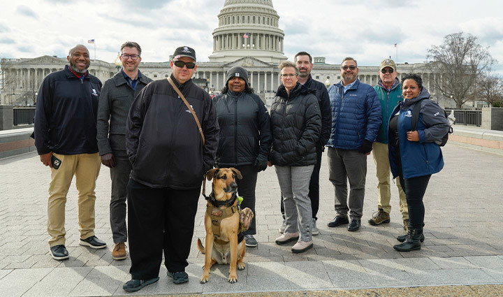 Several warriors, joined by a service dog, pose for a photo with the US Capitol in the background.