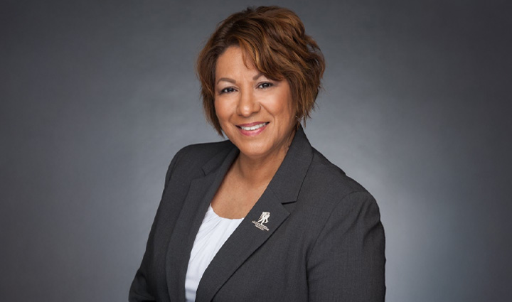 Caregiver Cindy Parsons poses, smiling, in a grey suit jacket with a Wounded Warrior Project pin on the lapel. 