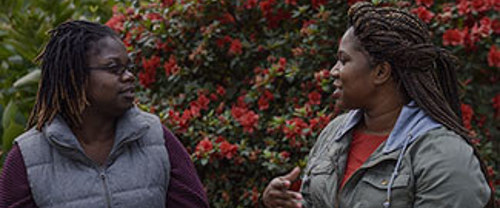 Two women talking outside in front of vibrant shrubbery