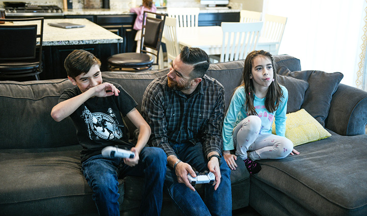 Warrior Arnulfo Dauto and his kids sit on their couch and laugh while playing video games together.