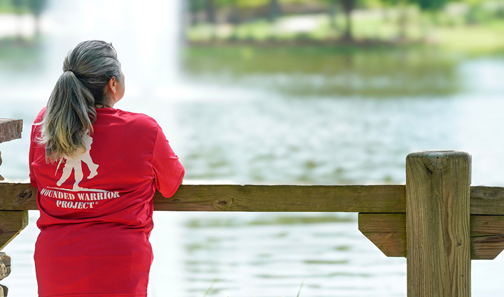 Warrior Maria Edwards stands in front of a water fountain with her back facing wearing a red WWP shirt.