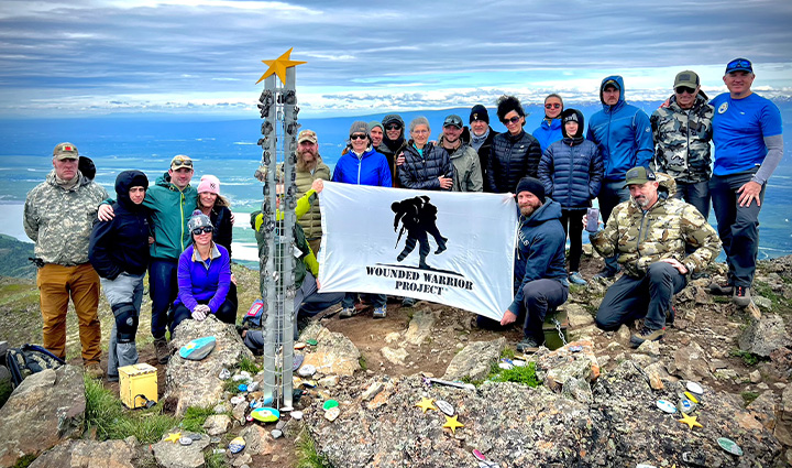 A group of people on a rocky mountain summit holding a Wounded Warrior Project flag.