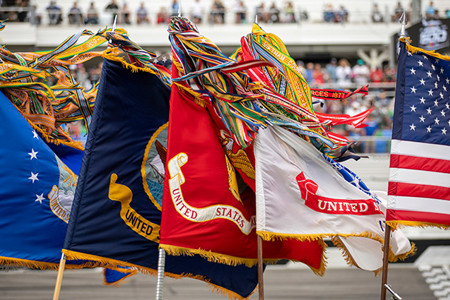 American and US military flags (Army, Marine, Navy, Air Force) are displayed outdoors, decorated with fringe and streamers.