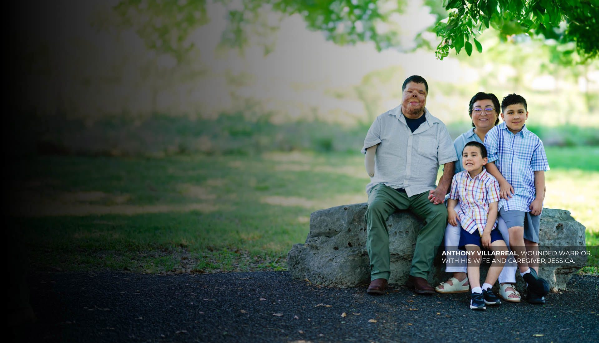 Warrior Anthony Villarreal sits with his wife & two sons under a tree. He has burn scars & his right arm amputated below elbow.