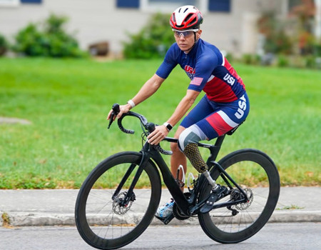 Warrior Kelly Elmlinger, proudly wears a USA national team Paratriathlon uniform, races on her bicycle with determination, her prosthetic leg moving her forward.