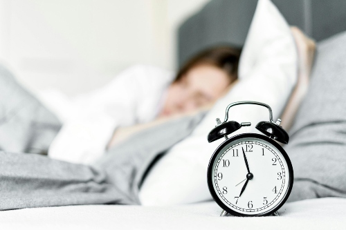 An alarm clock and a person sleeping. Sleep issues can lead to greater irritability and affect physical stamina, cause weight gain, and lead to challenges in managing other chronic health conditions.