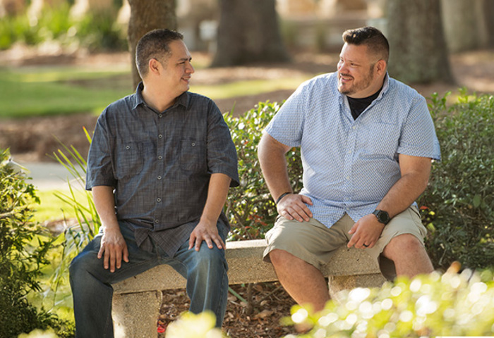 Wounded warriors Jason Major and Jacob Norotsky sit outside on a bench smiling and talking to each other.