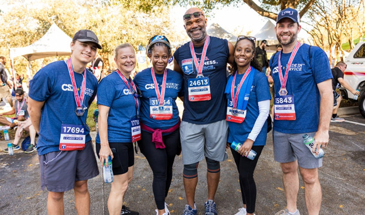 Three men and three women, all CSX employees, are dressed in blue t-shirts and standing together. They are smiling after completing the WWP Carry Forward 5K.