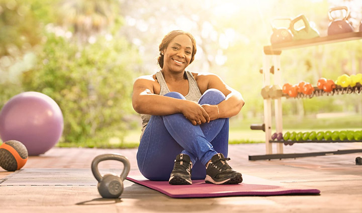 Wounded warrior Yolanda Poullard sits on a yoga mat with her legs crossed, surrounded by various workout gear, such as weights and exercise balls.