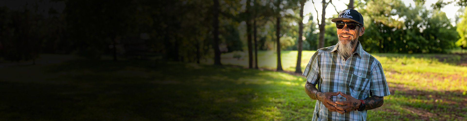 Wounded warrior Ray Andalio standing in a park, smiling and wearing sunglasses and a WWP hat.