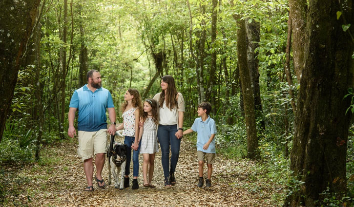 Wounded warrior Issac Malone with his wife Jenna Malone and children and service dog walking in the woods.