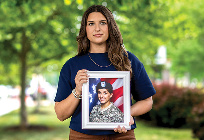 Warrior Keara Torkelson holding a framed military portrait in front of a blurred green outdoor setting.