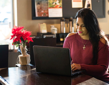 Warrior Yomari Cruz sitting at a table and looking at her computer.