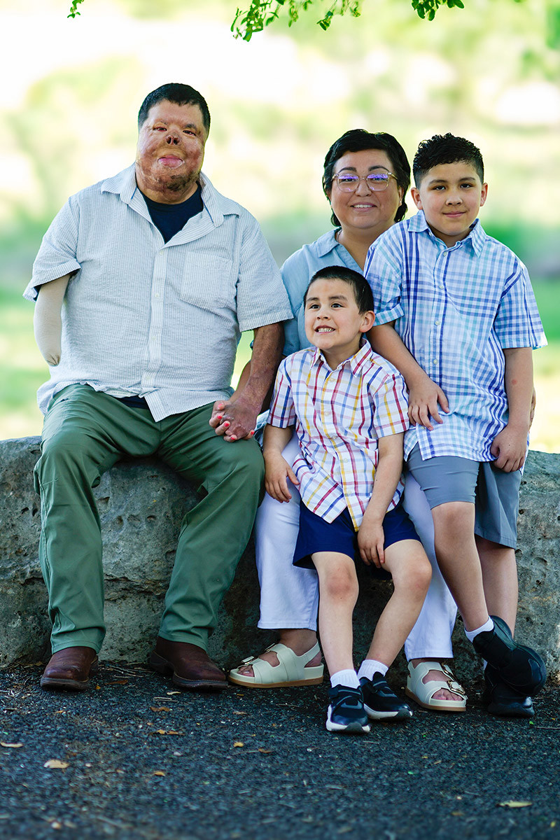Wounded warrior Anthony Villareal, his wife, and two sons sit on a large rock while smiling at the camera. Anthony holds his wife’s hands as both children sit on her lap.