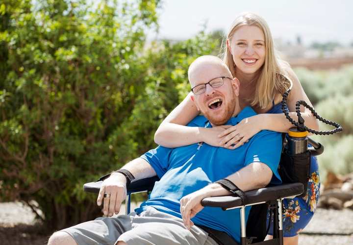 Wounded warrior Erik Schei sits in his wheelchair while his sister Anneka hugs him from behind.