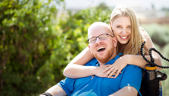 Wounded warrior Erik Schei sitting in a wheelchair and smiling while his sister Anneka hugs him.