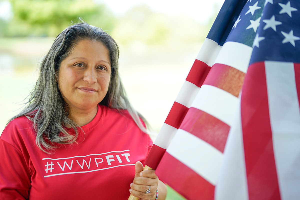 Wounded warrior Maria Edwards smiles softly at the camera while holding an American flag.
