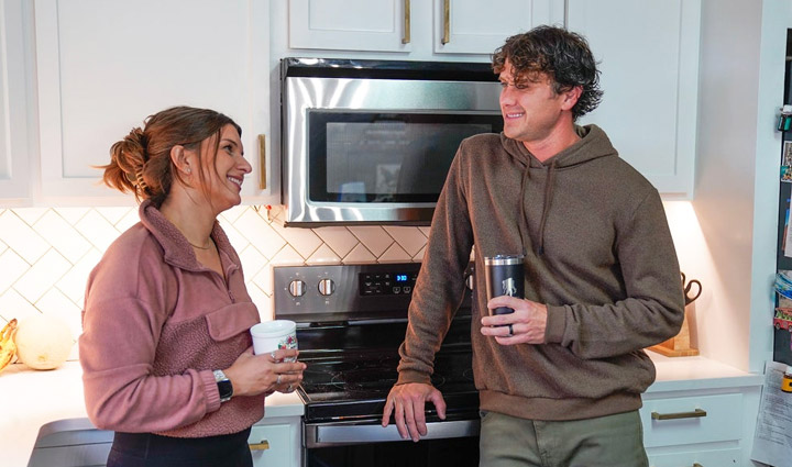 Wounded warrior Keara Torkelson and her husband stand in their kitchen, holding coffee mugs, and smiling at each other. 