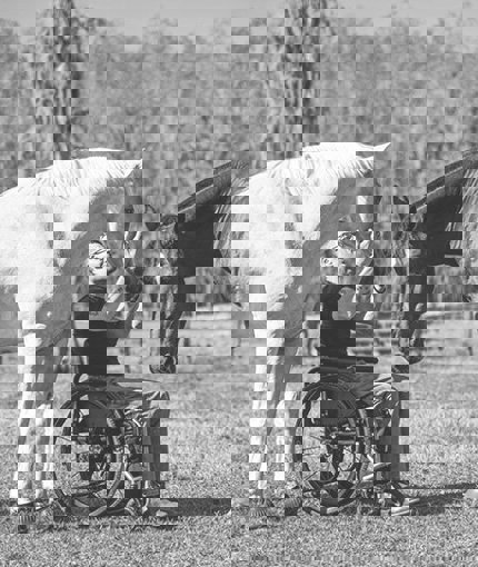 Wounded warrior Mark Lalli sitting on a wheelchair at Quantum Leap Farm while petting horses.